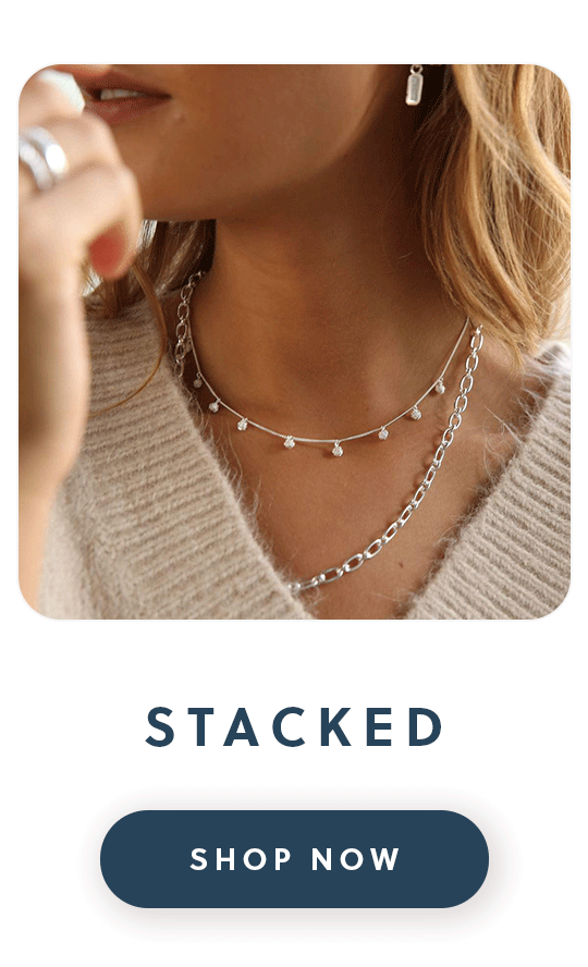 A close up of a woman wearing two Daisy London Stacked necklaces with text stacked shop now