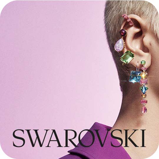 Woman wearing vibrant Swarovski earrings, purple background